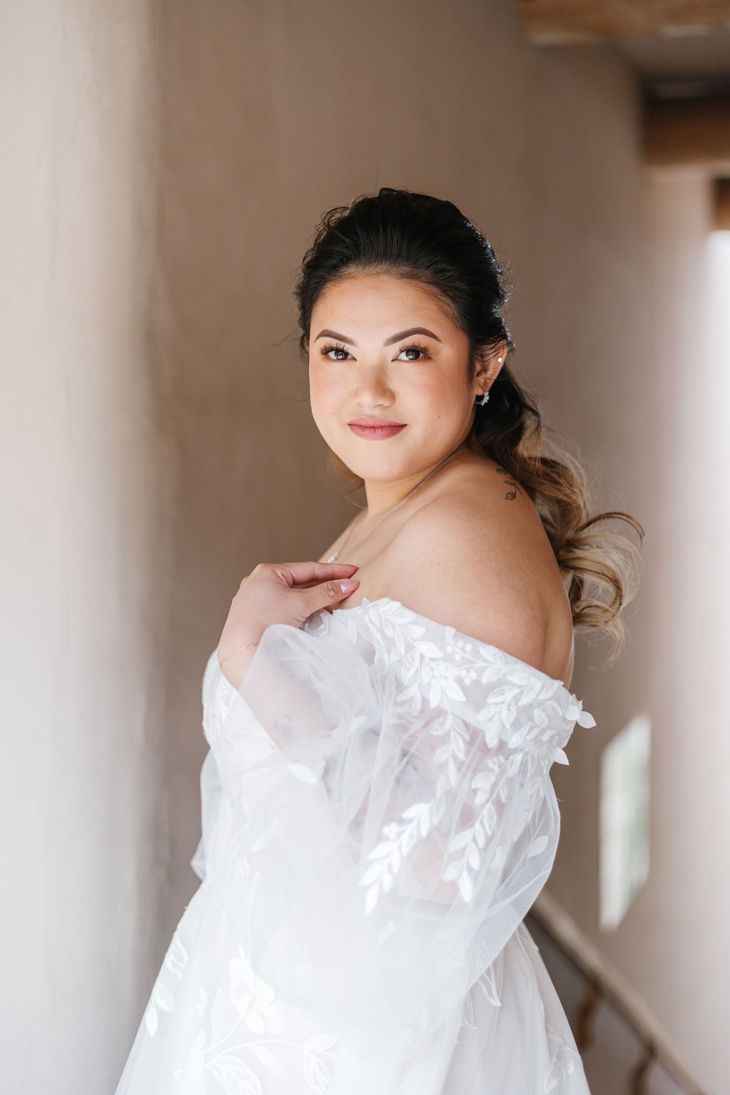 A bride in a white off-shoulder wedding dress poses elegantly in a bridal portrait series.