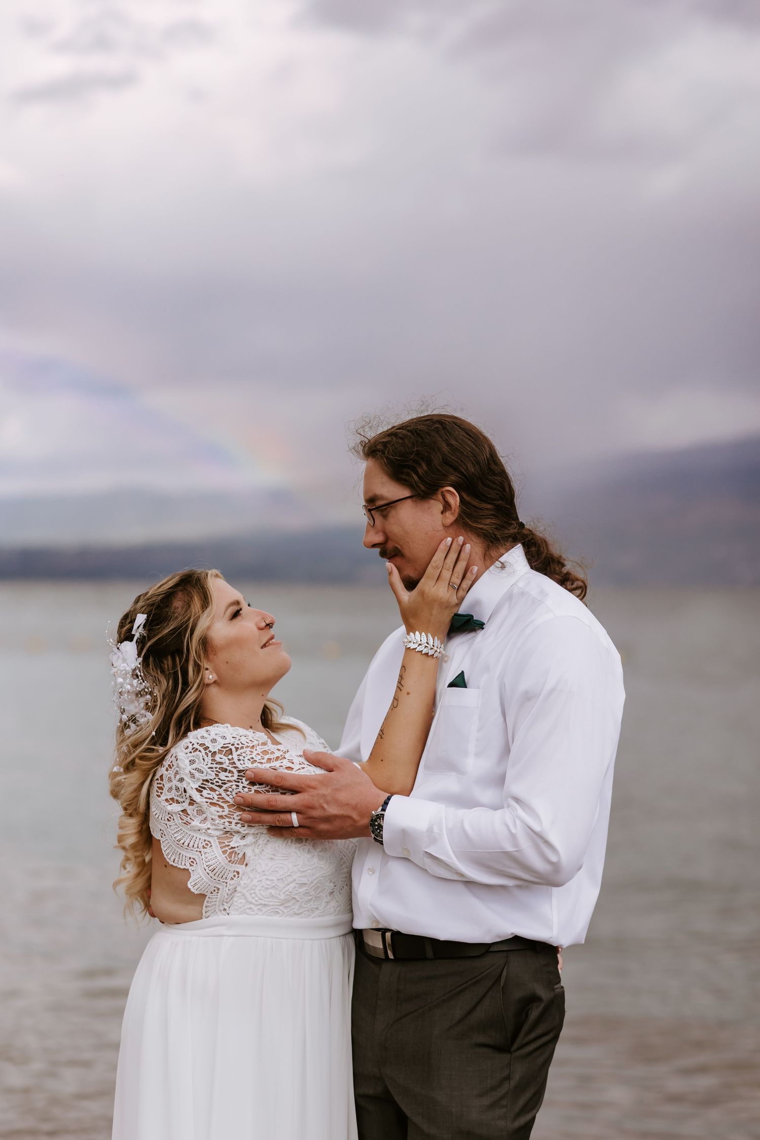 A romantic couple shares tender moments by the water during their wedding photo session on a cloudy day.
