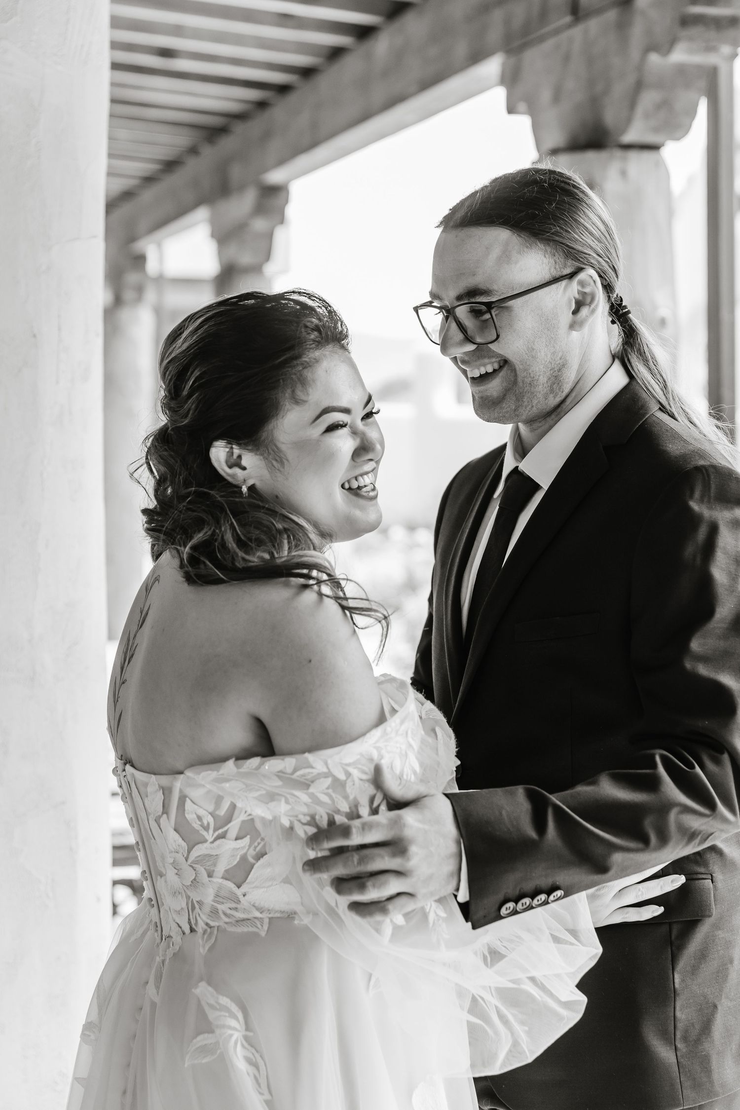 Black and white wedding photos showing a couple embracing and laughing together under white columns.