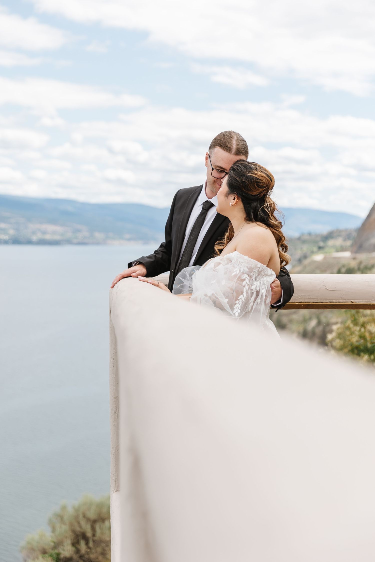 Romantic wedding moment captured against a scenic mountain and lake backdrop on a cloudy day.