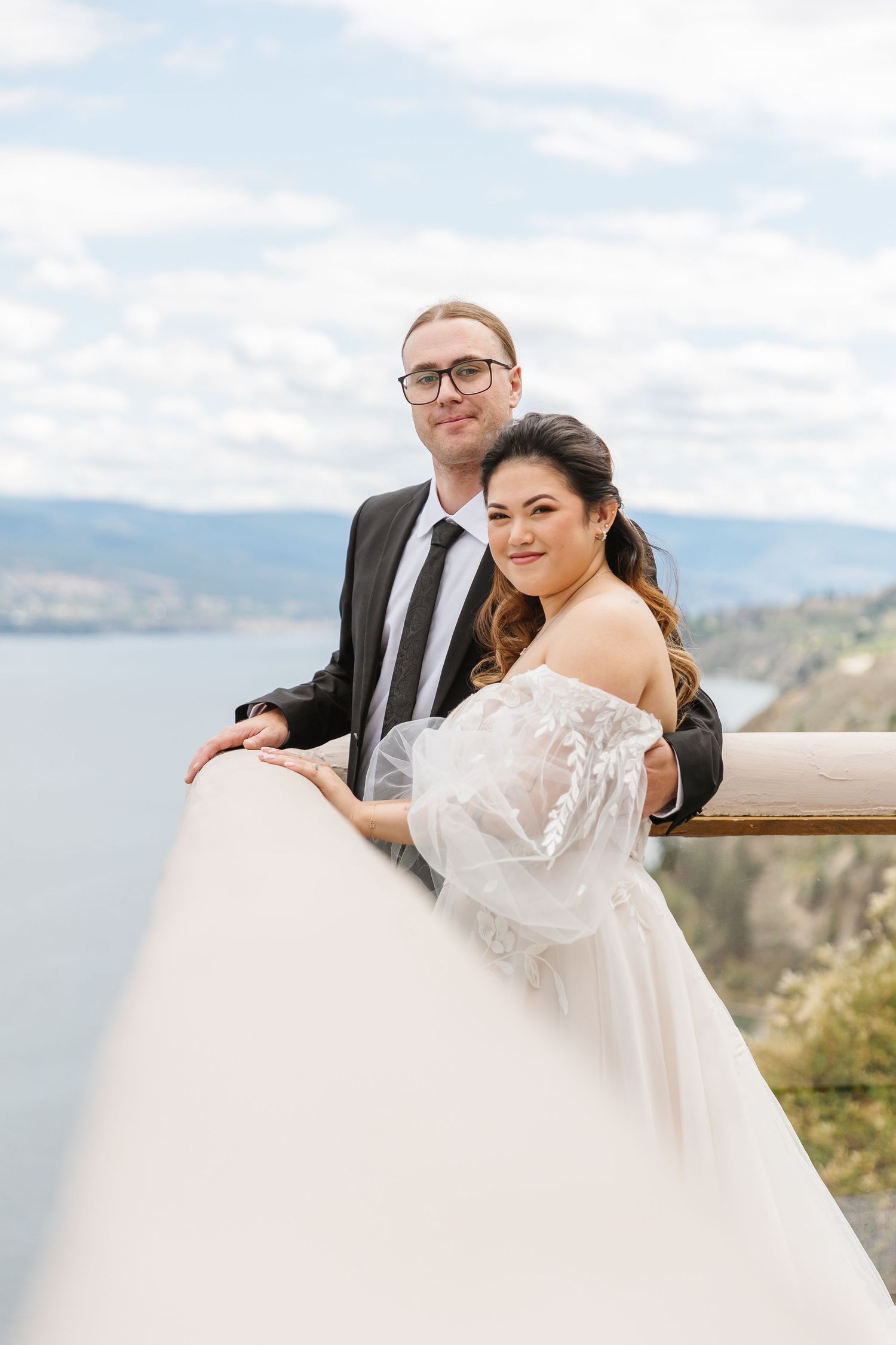 A wedding couple posing for romantic portraits against a scenic mountain lake backdrop.