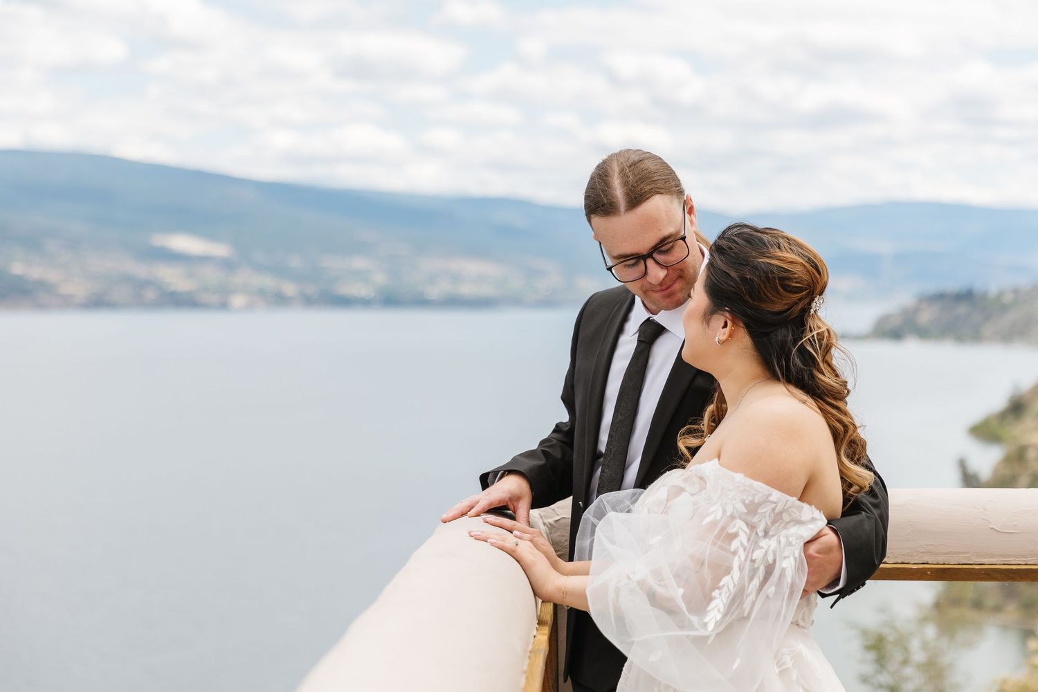 Romantic wedding couple embraces while overlooking scenic mountain lake on their special day.