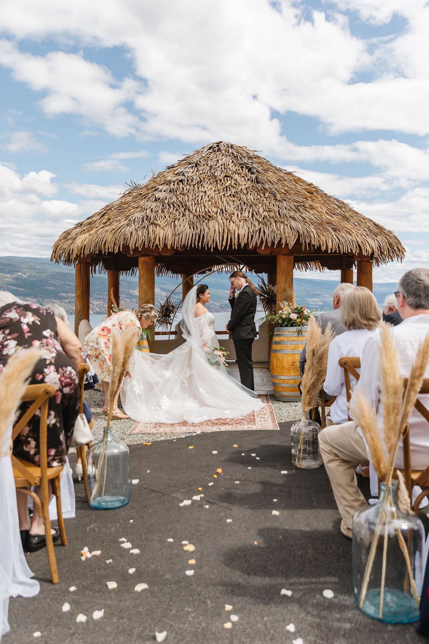 Outdoor beach wedding ceremony under thatched roof gazebos with mountain and lake views.