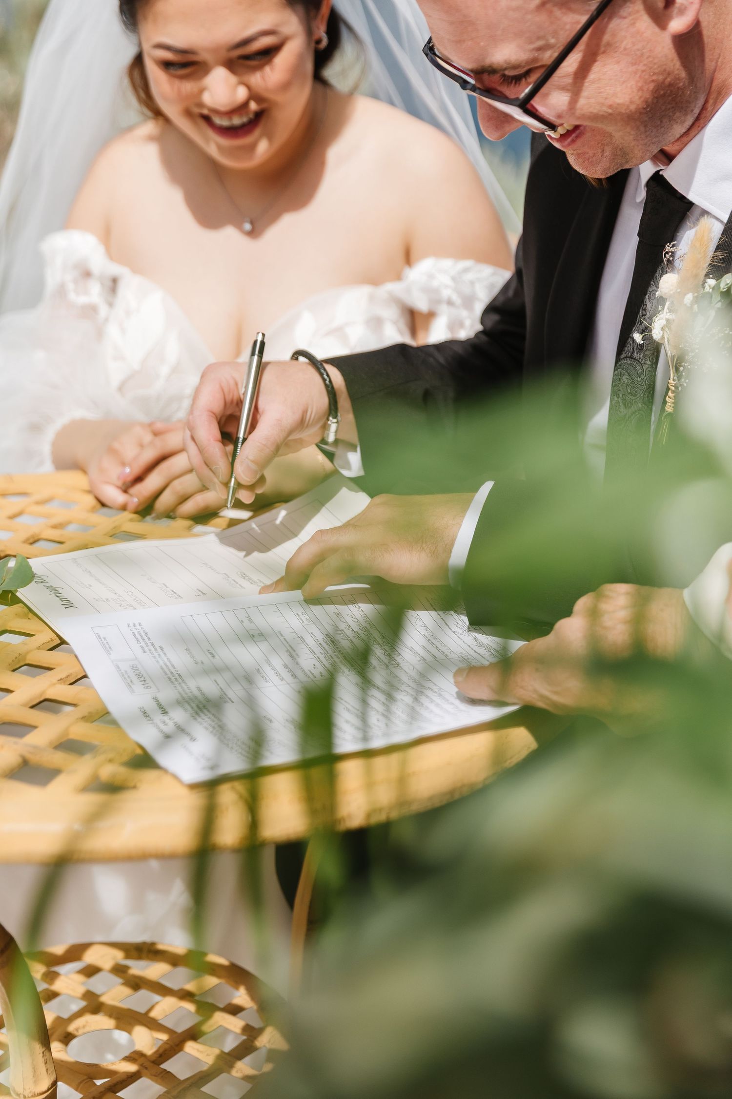 Wedding couple signing marriage documents together at an outdoor reception.