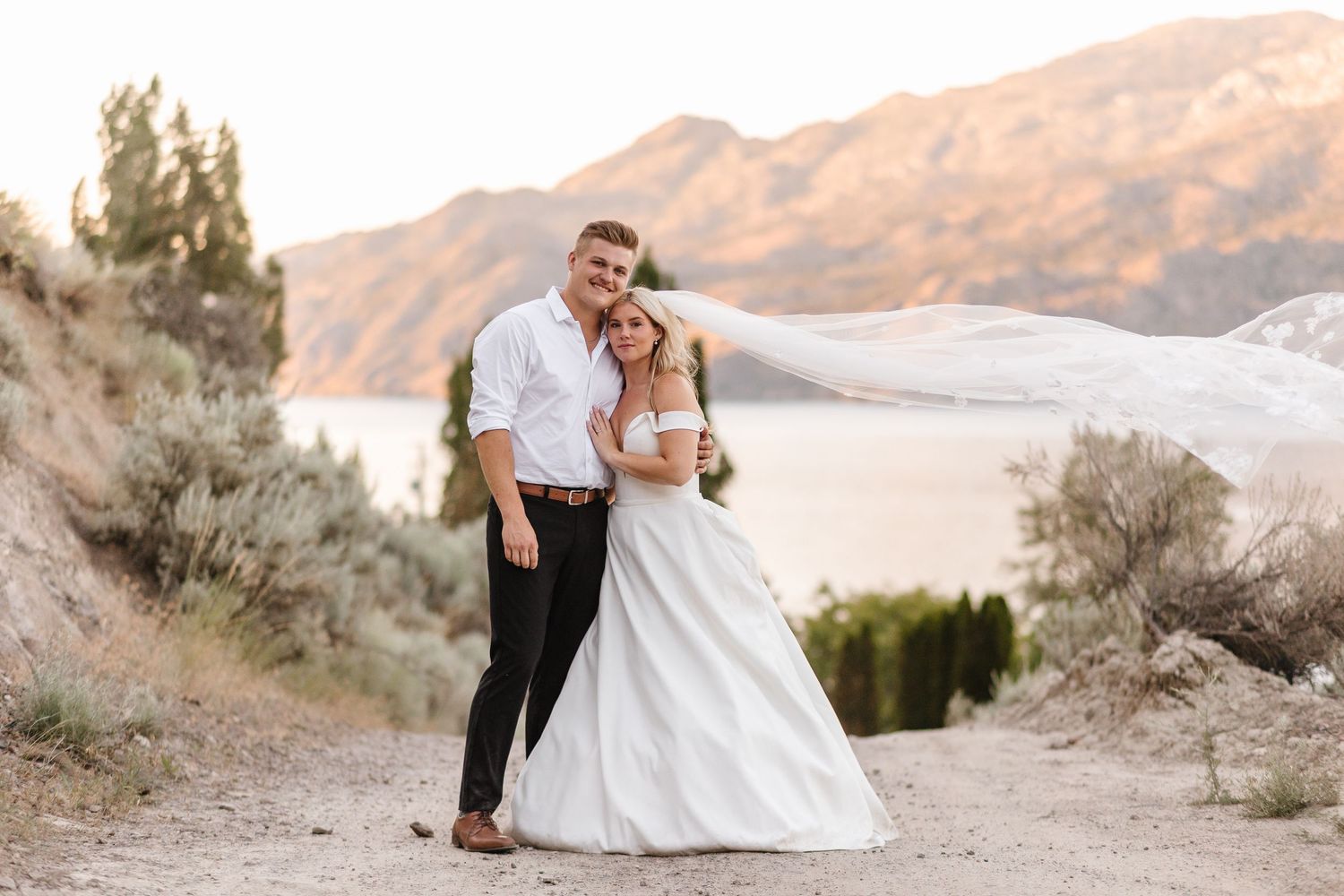 A couple shares a romantic moment against a desert mountain backdrop during their wedding photo session at sunset.