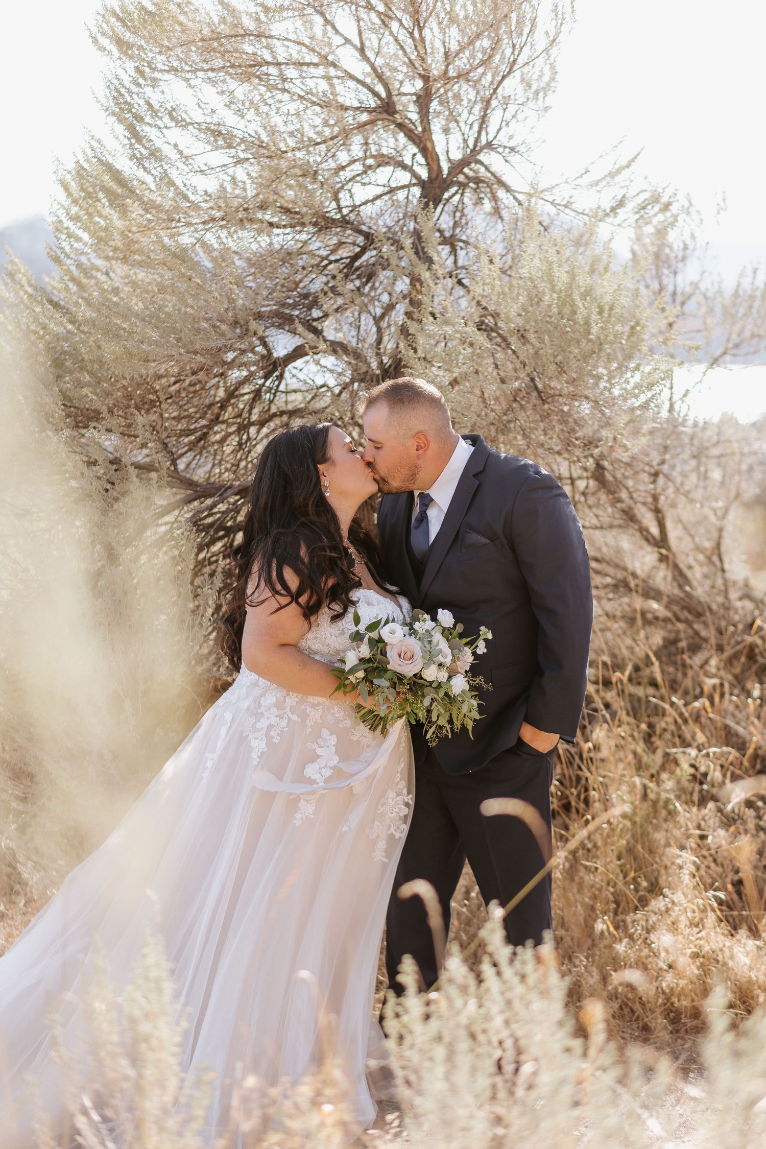Romantic wedding couple shares intimate moments among golden desert brush at sunset.
