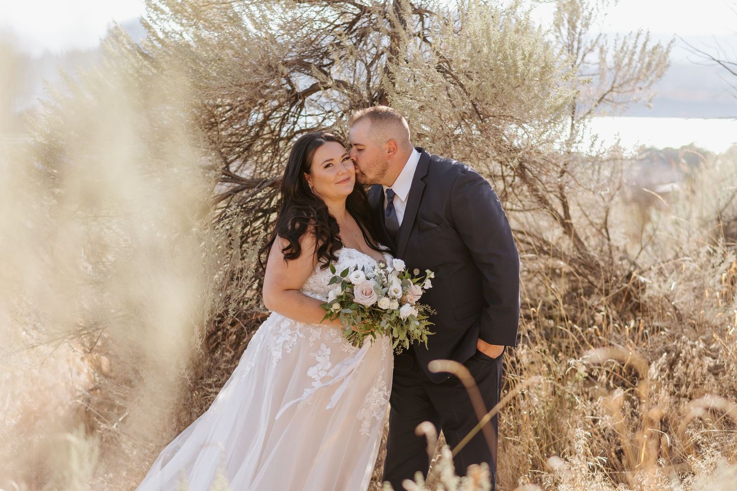 A romantic wedding couple shares tender moments in a rustic outdoor setting with natural desert scenery.