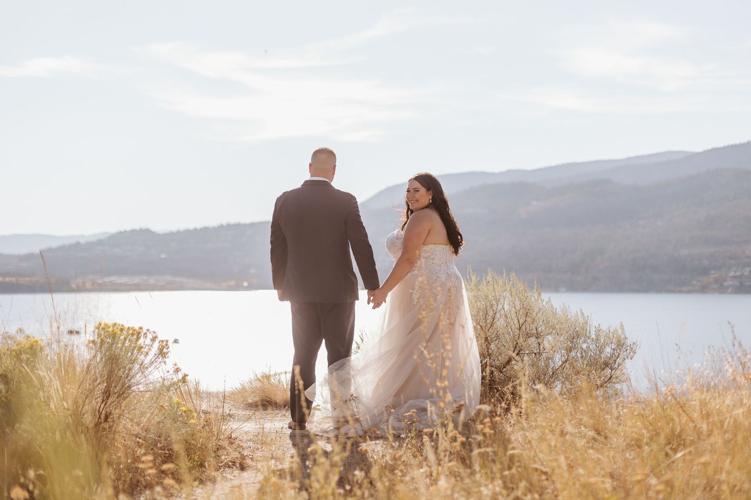 A couple sits together on a hilltop overlooking a scenic lake view during golden hour.