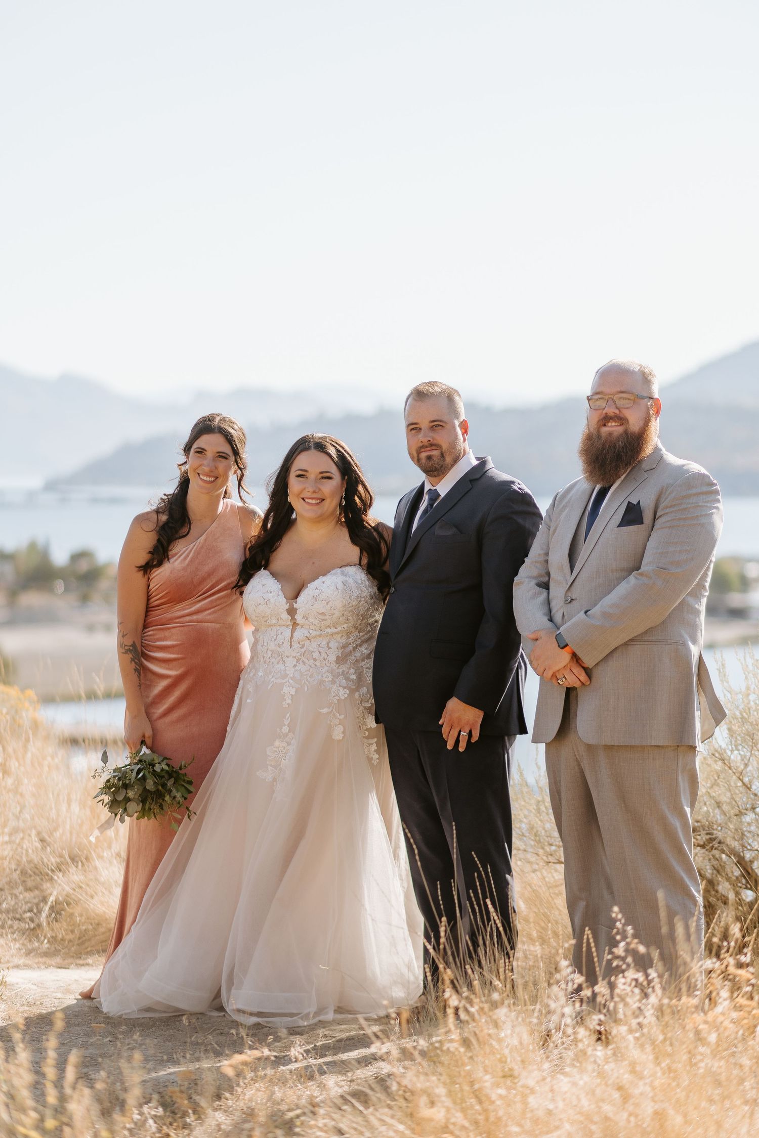 Wedding party poses together in golden field with mountains in background during sunset ceremony.