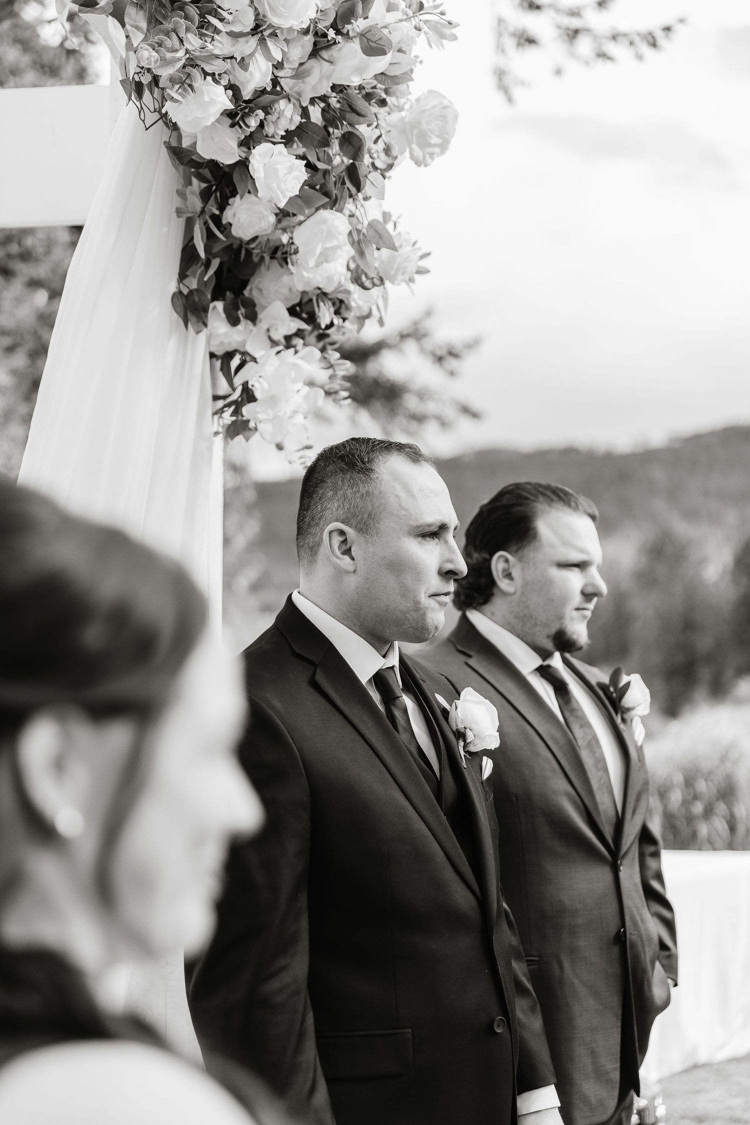 Black and white photo of groomsmen standing in a line during an outdoor wedding ceremony.