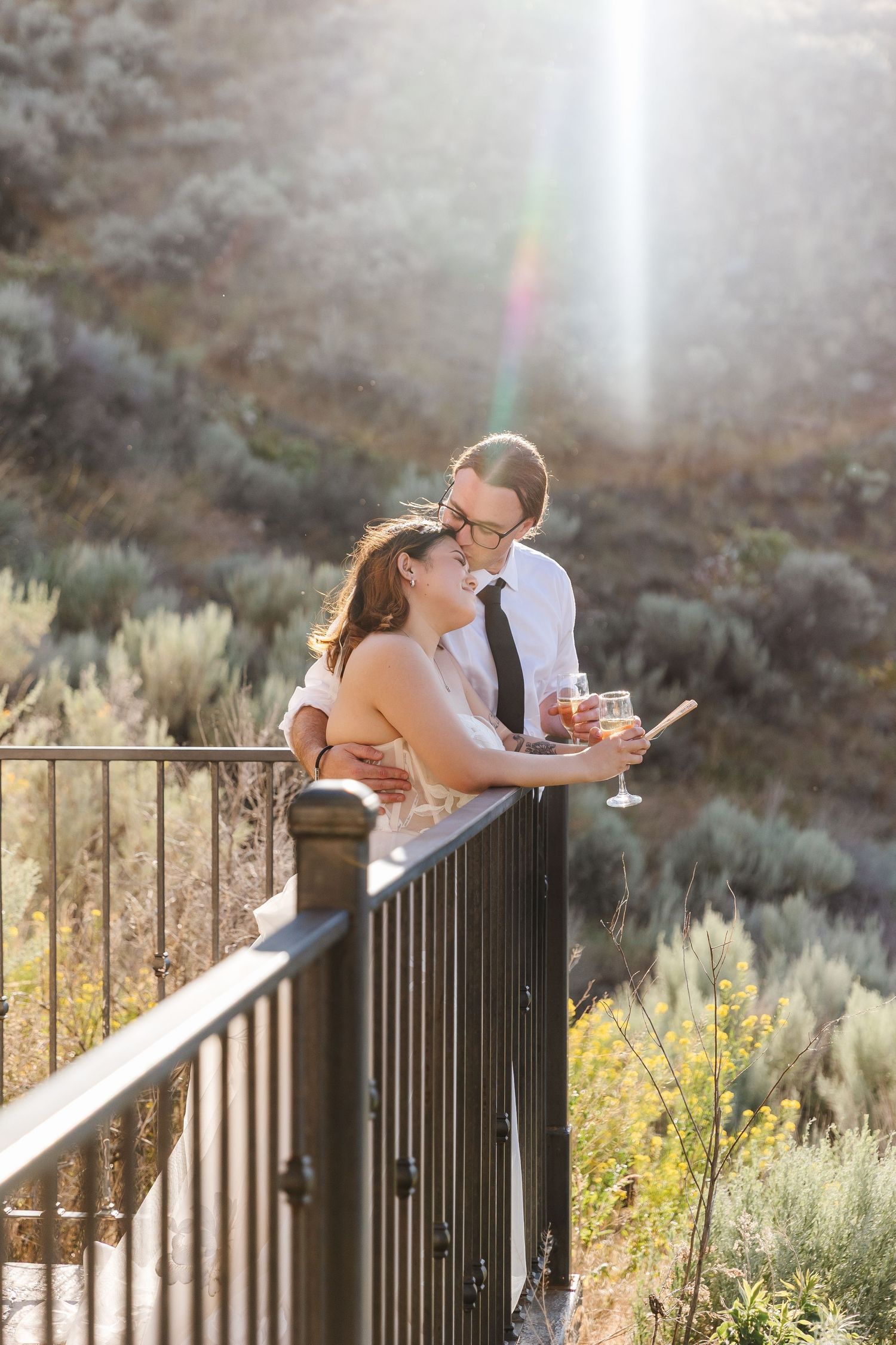 Romantic couple sharing a drink on a mountain overlook deck during golden hour sunset.