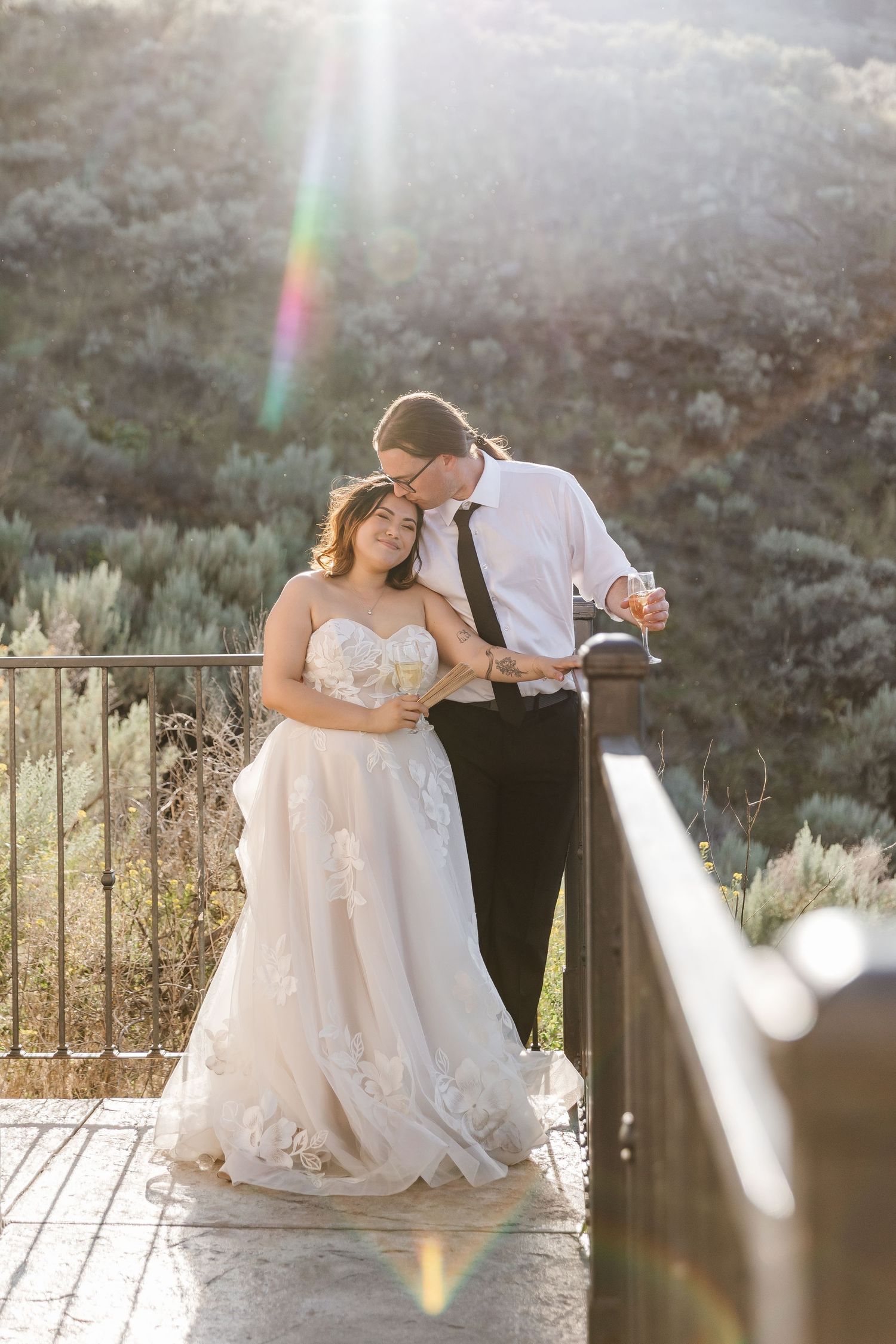 Newlyweds sharing an intimate moment on a balcony with sunlight creating a beautiful lens flare.