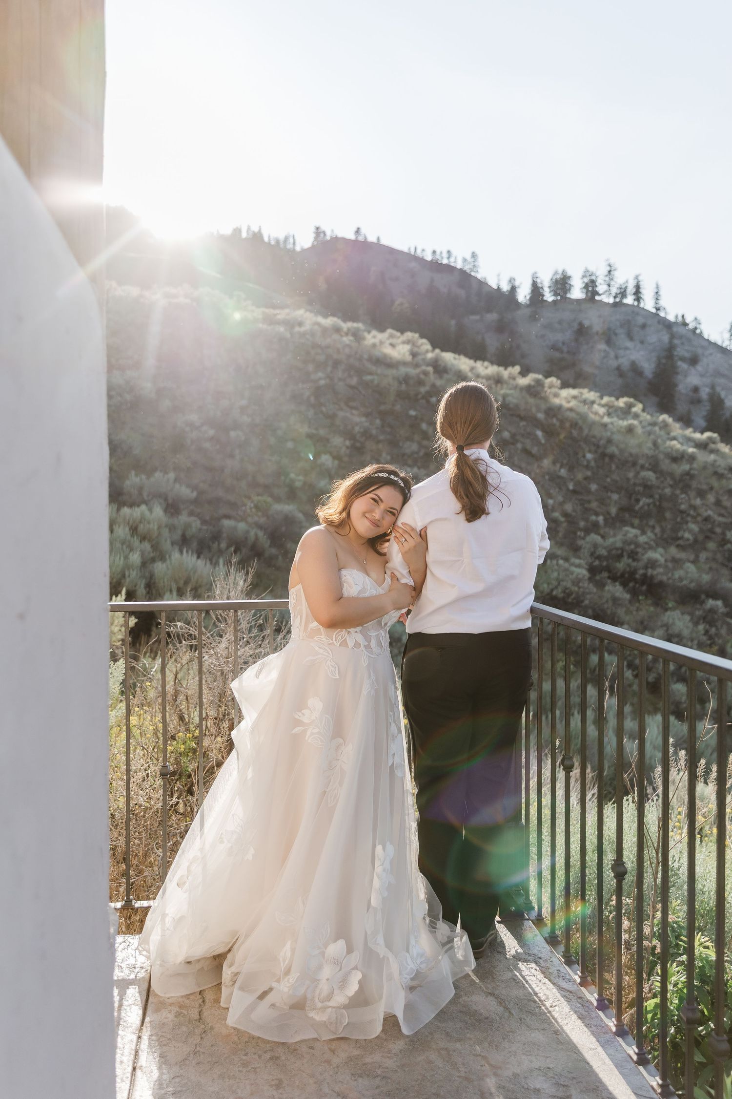 Wedding couple embracing on a scenic mountain balcony with sunlight streaming through.