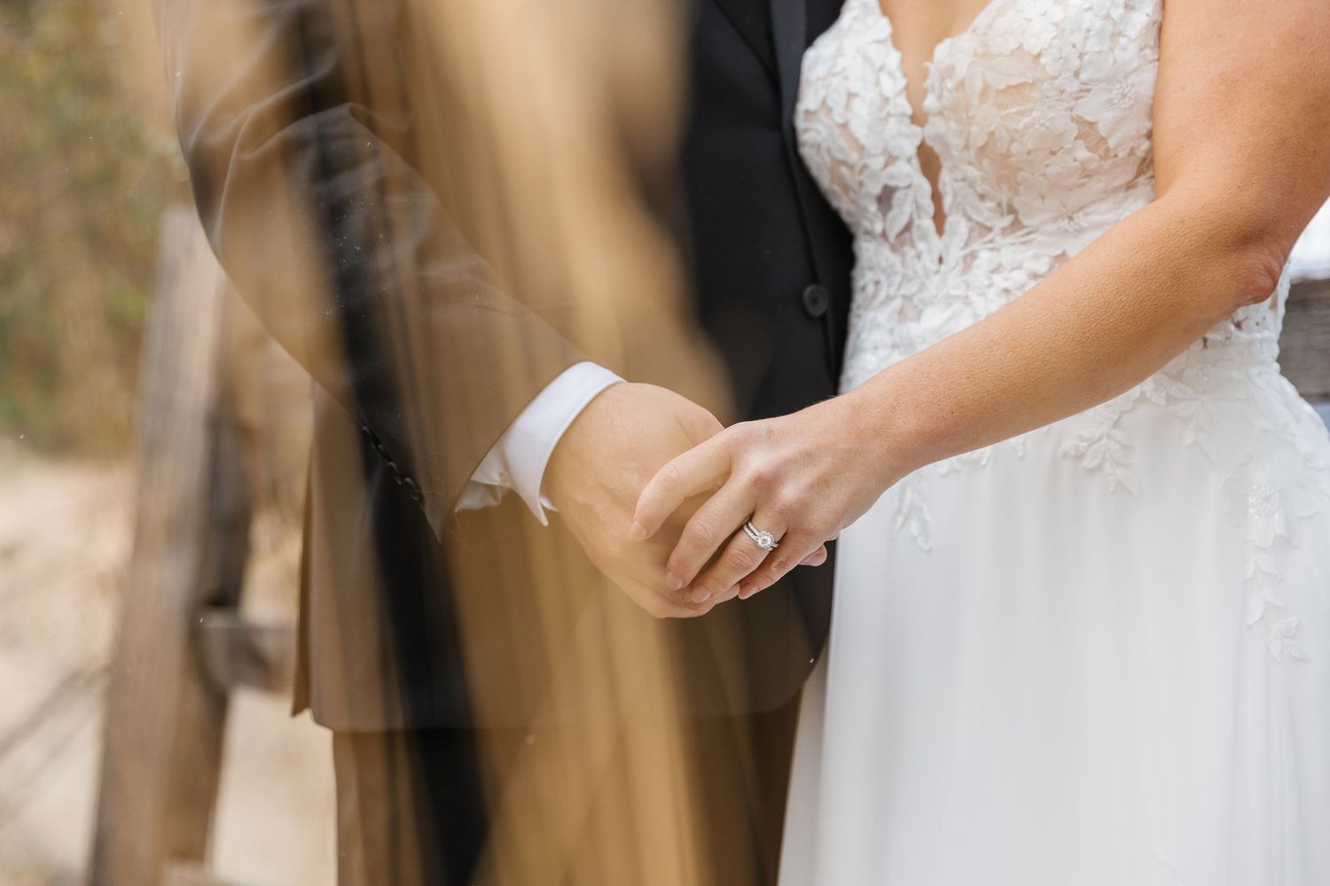 A bride in a white lace wedding dress holds a bouquet of white and pink flowers in a forest setting.