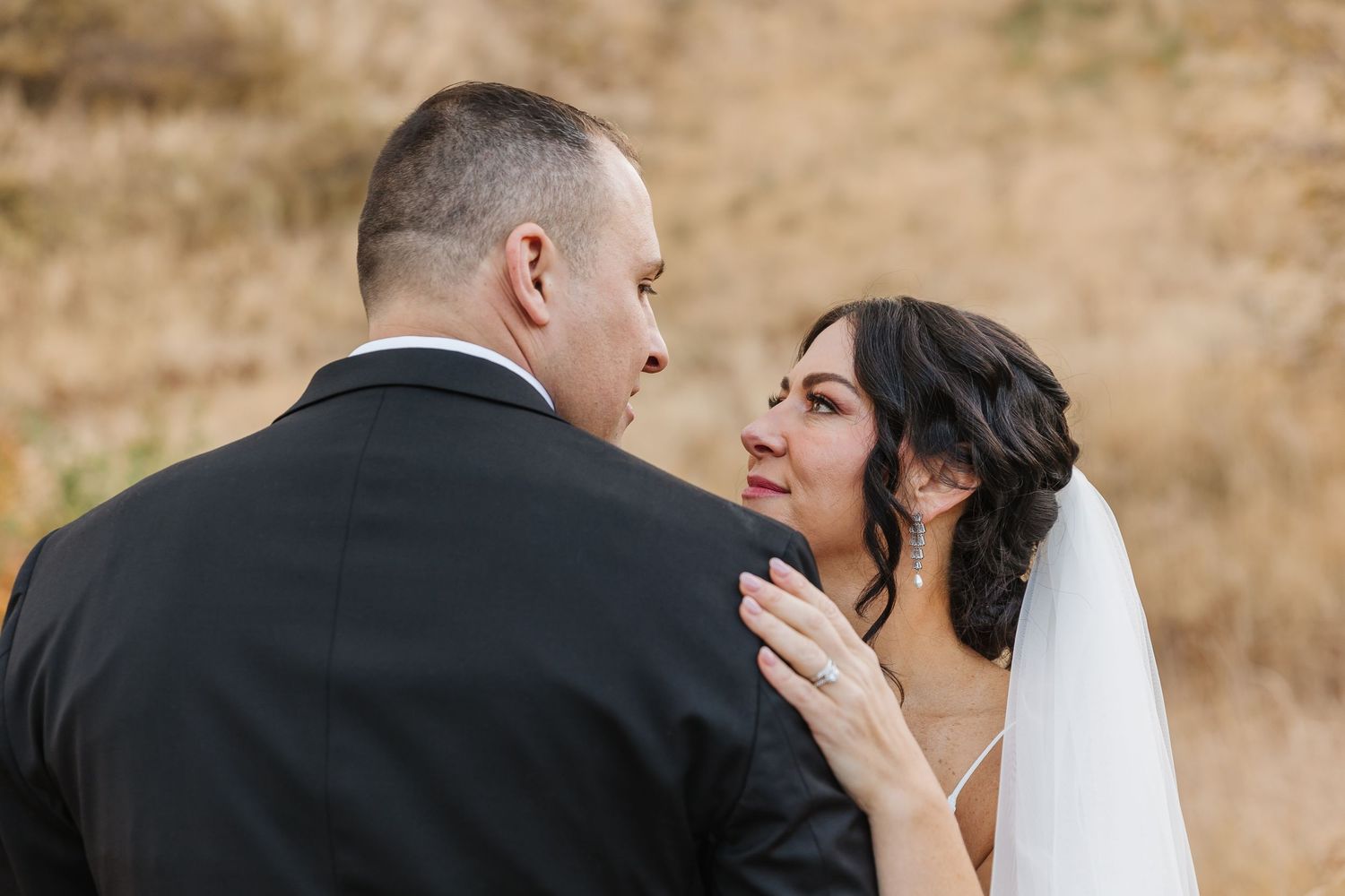 A bride and groom share an intimate moment during their wedding photoshoot against a rustic outdoor backdrop.
