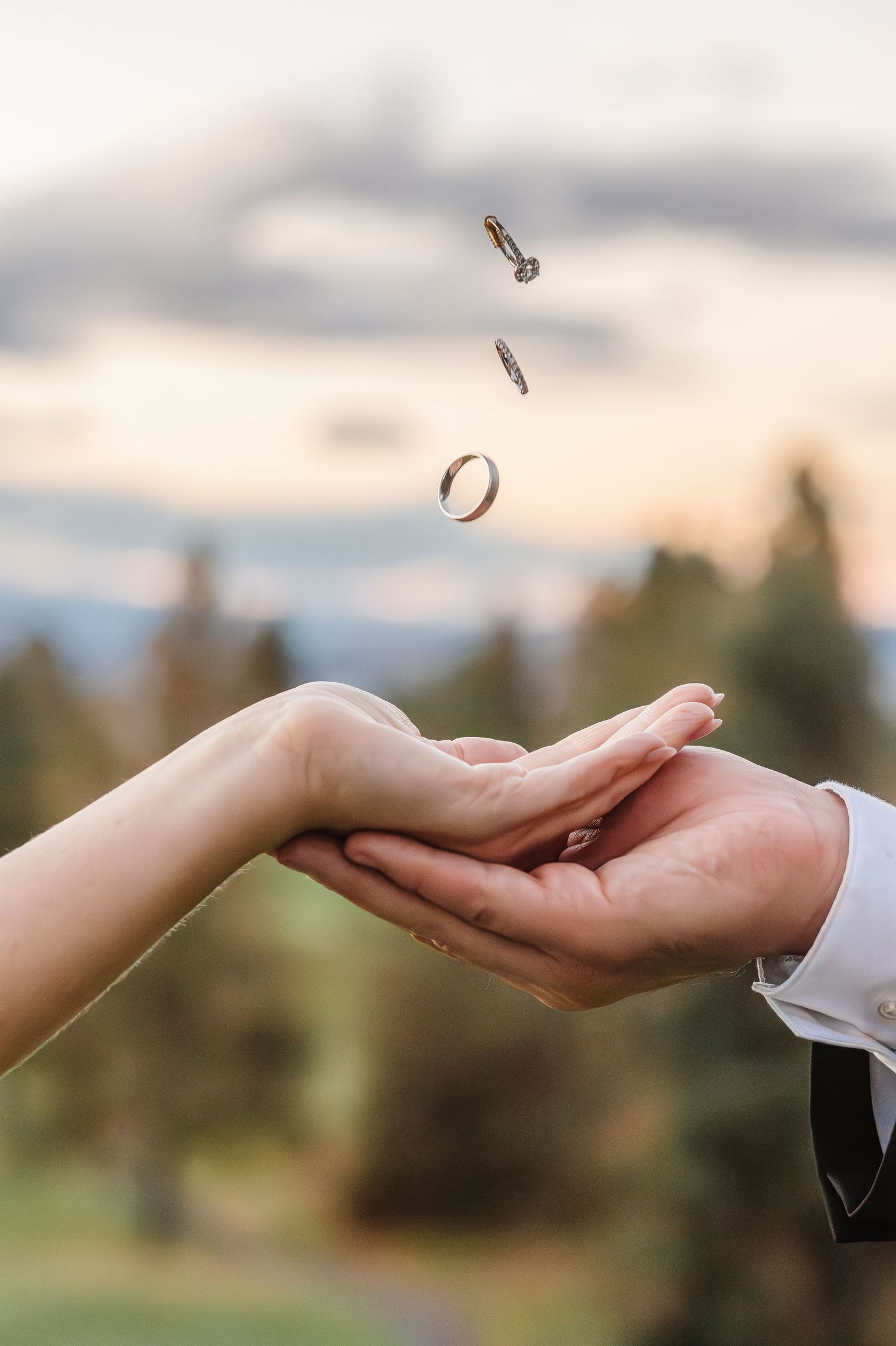 Wedding rings being tossed between hands against a blurred natural outdoor background during sunset.