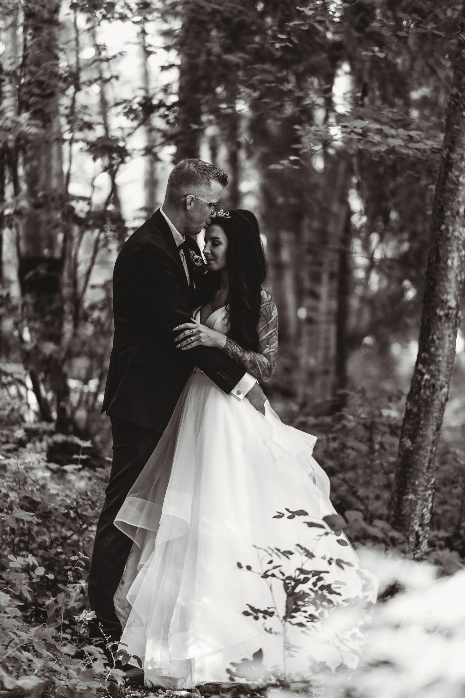 A romantic black and white wedding photo of a couple embracing in a misty forest setting.