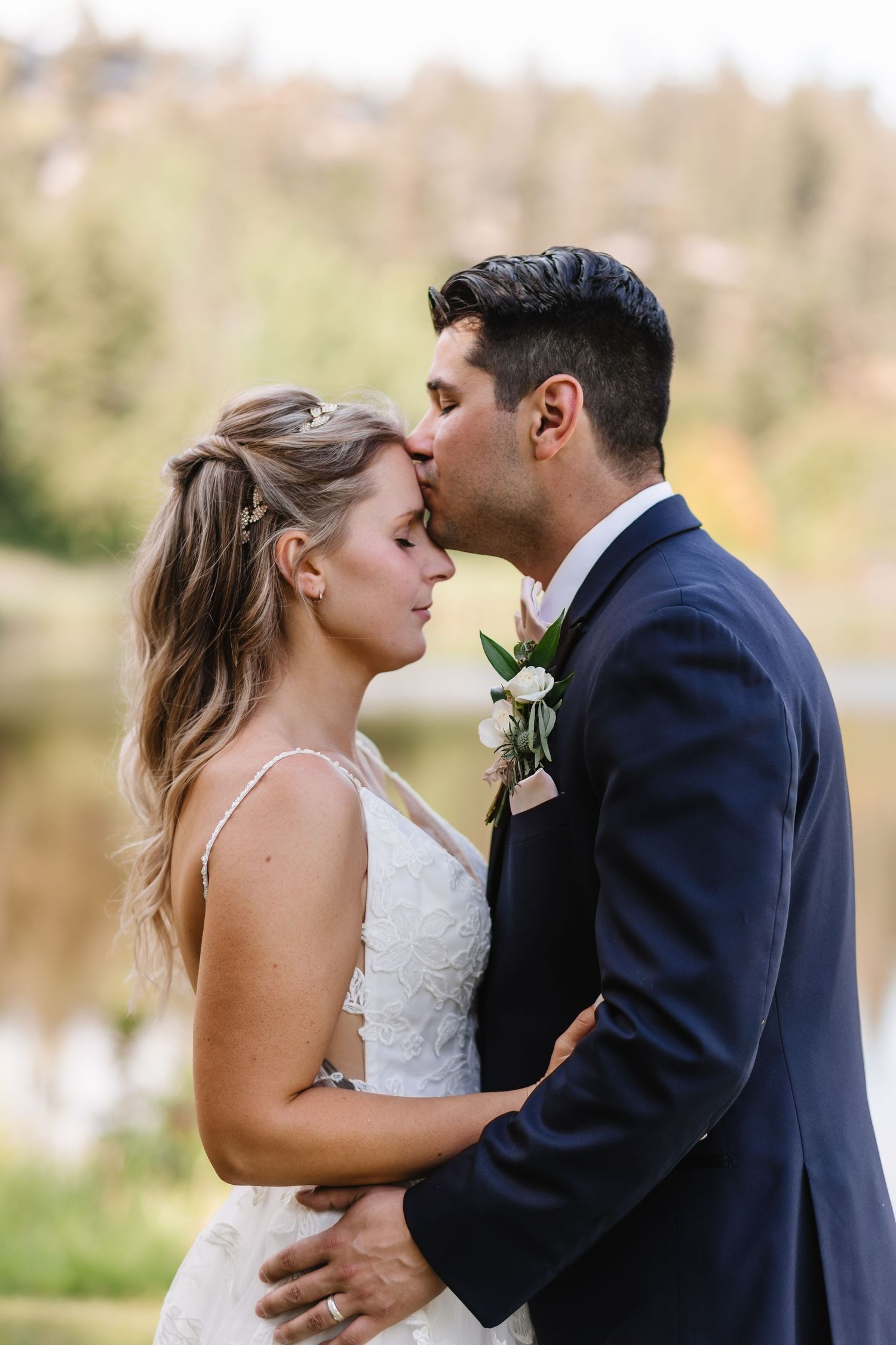 A bride and groom share intimate moments during their outdoor wedding photo session near a lake.
