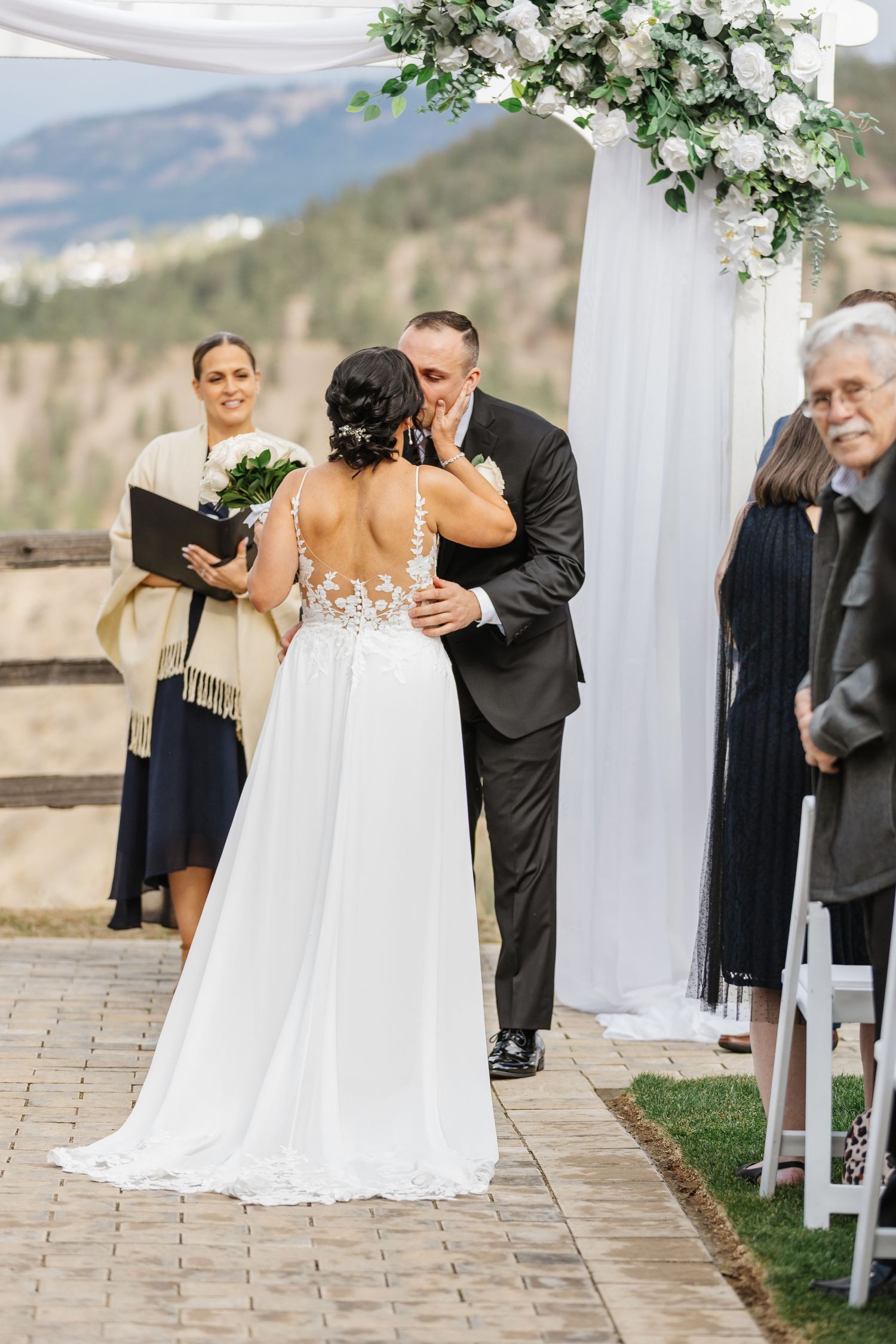 Emotional first look sequence between family members at an outdoor wedding with white floral arrangements.