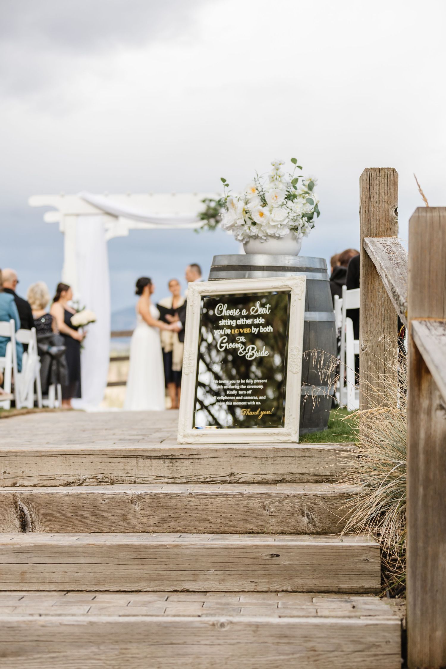 Wedding decor and signage displayed on wooden steps with guests visible in the background.