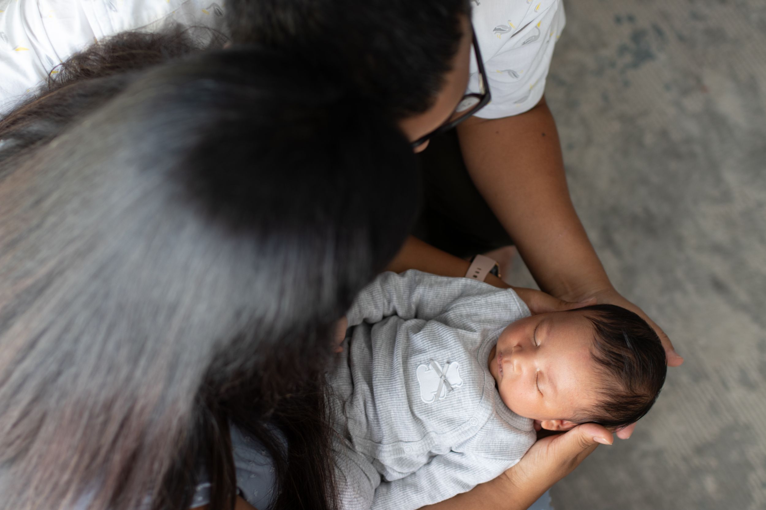 A mother tenderly holds her sleeping newborn baby wrapped in a gray swaddle blanket.