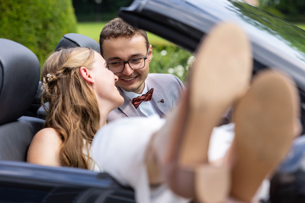 A romantic moment between newlyweds in a convertible car with feet visible.