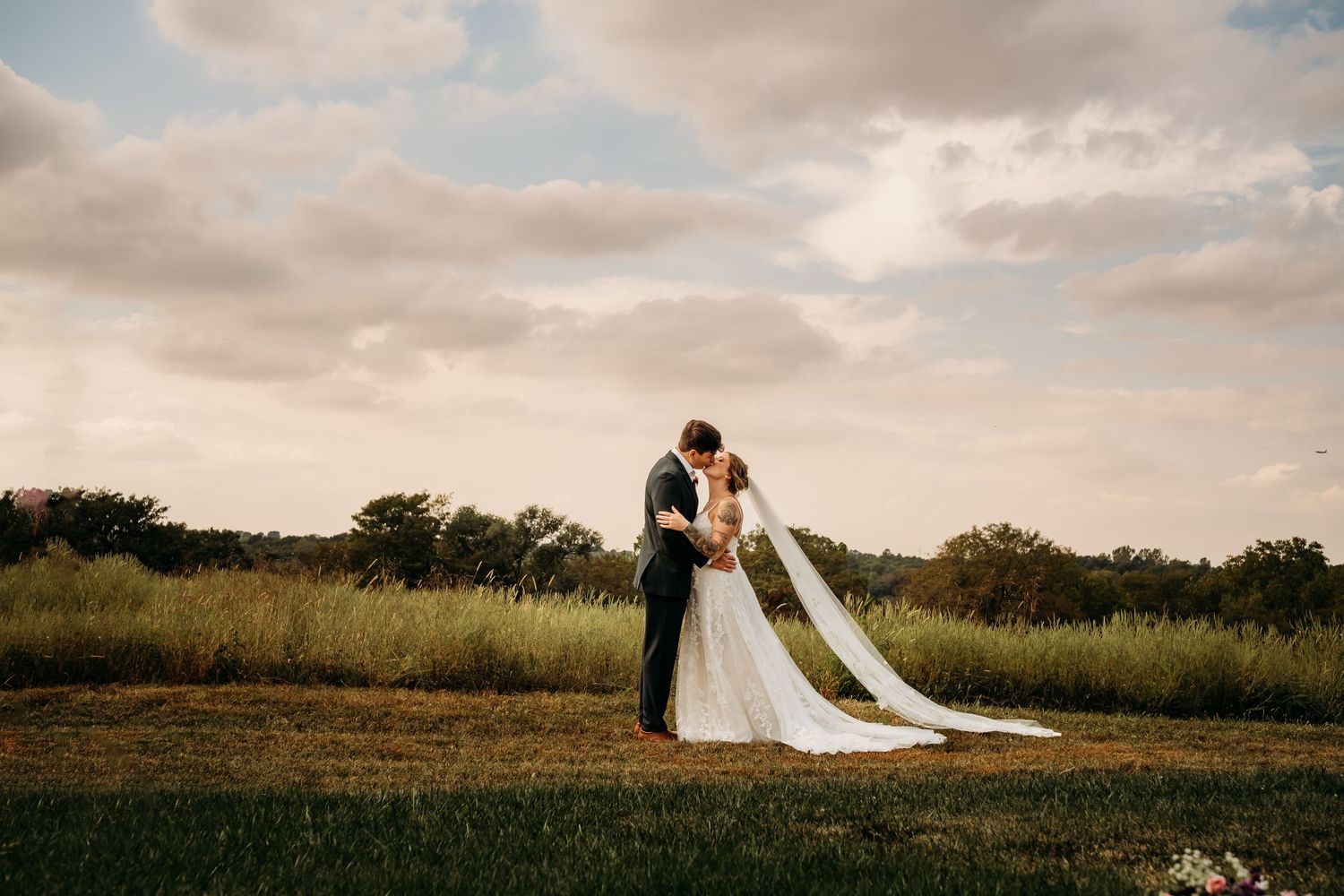 Couple kisses in wedding attire in front of a field during elopement in Kansas City, Missouri