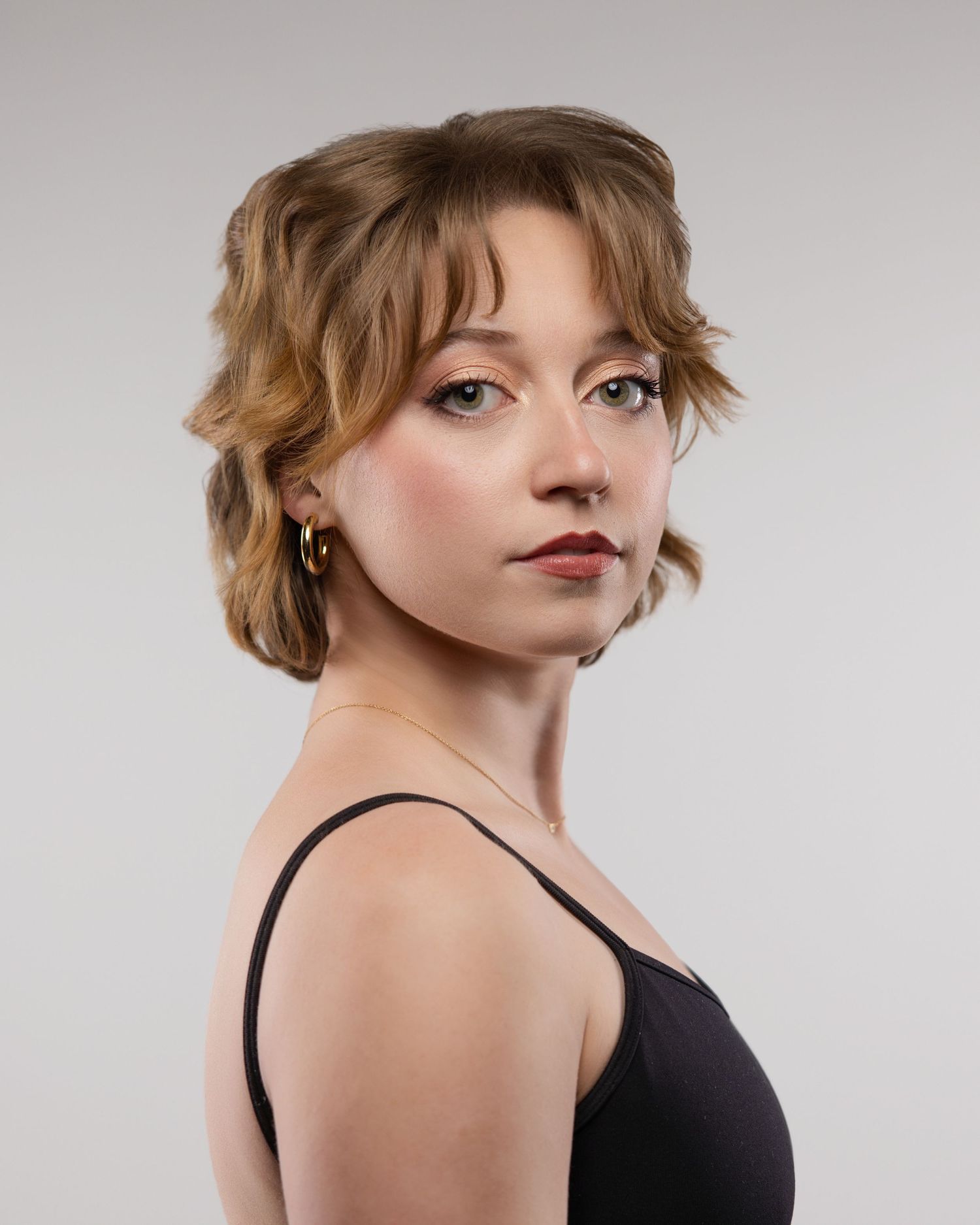Portrait of someone with honey-blonde hair wearing a black tank top against a neutral gray background.