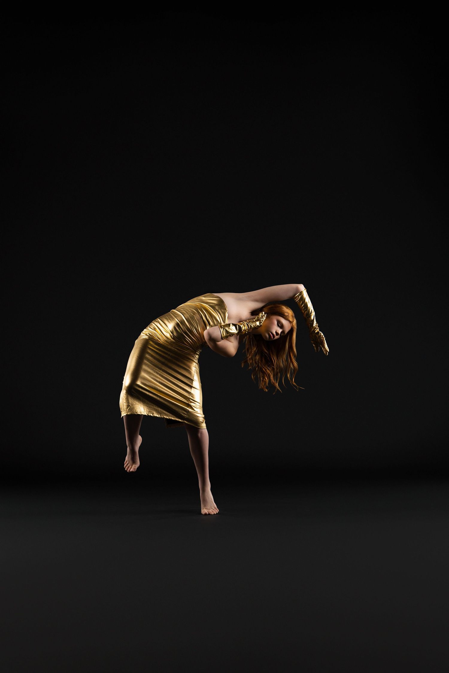 A woman in a gold metallic dress strikes a dramatic dance pose against a dark background.