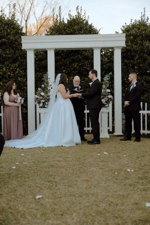 Wedding ceremony taking place under white pergola with guests watching.