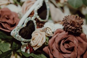 Wedding rings and floral details with mauve roses and dried flowers in an artistic macro shot.