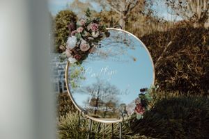 Decorative round mirror with floral arrangements reflecting a garden setting.