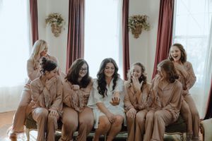 Bridesmaids in matching silk robes sharing a laugh during wedding preparations.