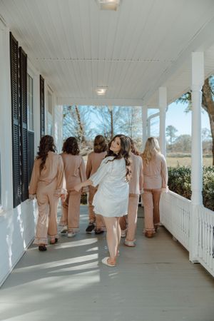 Wedding party in matching robes walking along a white porch.