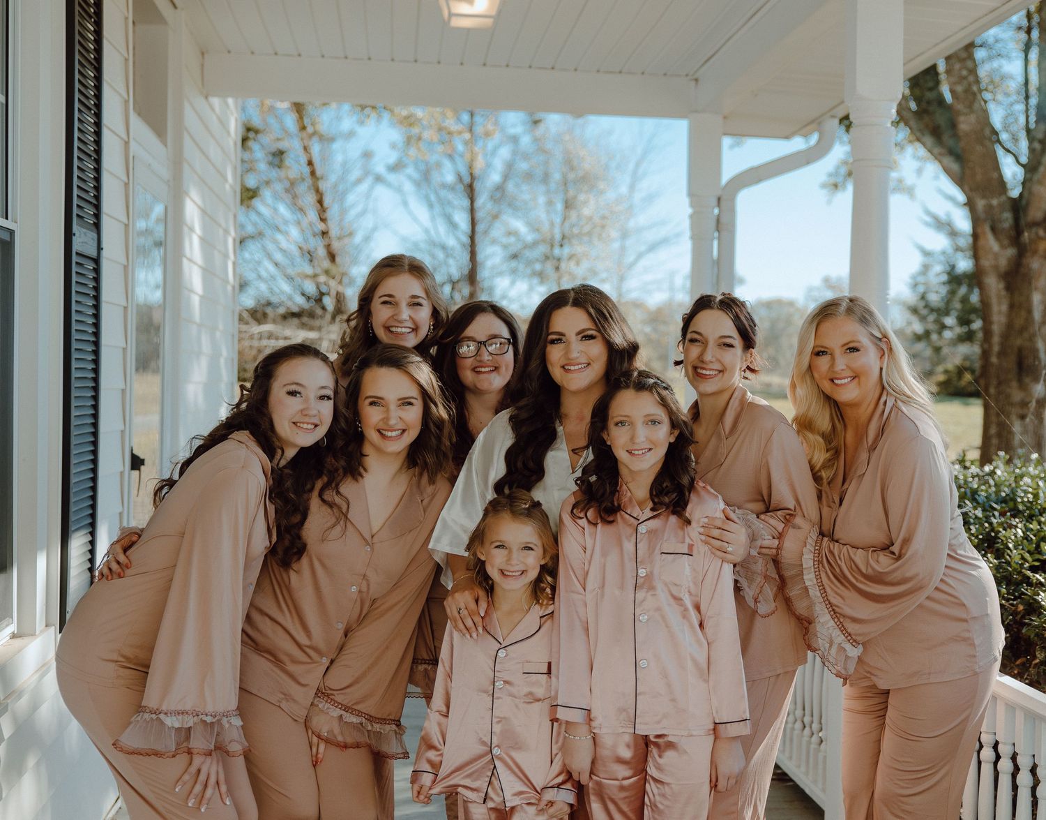Bridal party in matching blush robes posing on a porch.