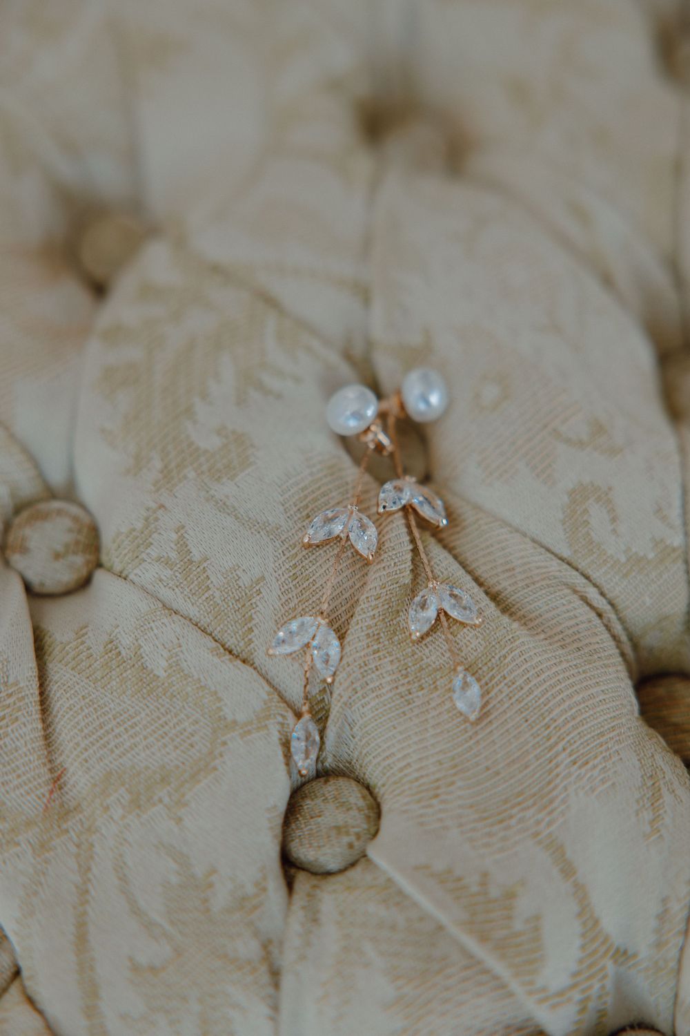 Delicate wedding jewelry and accessories arranged on a textured cream-colored fabric.