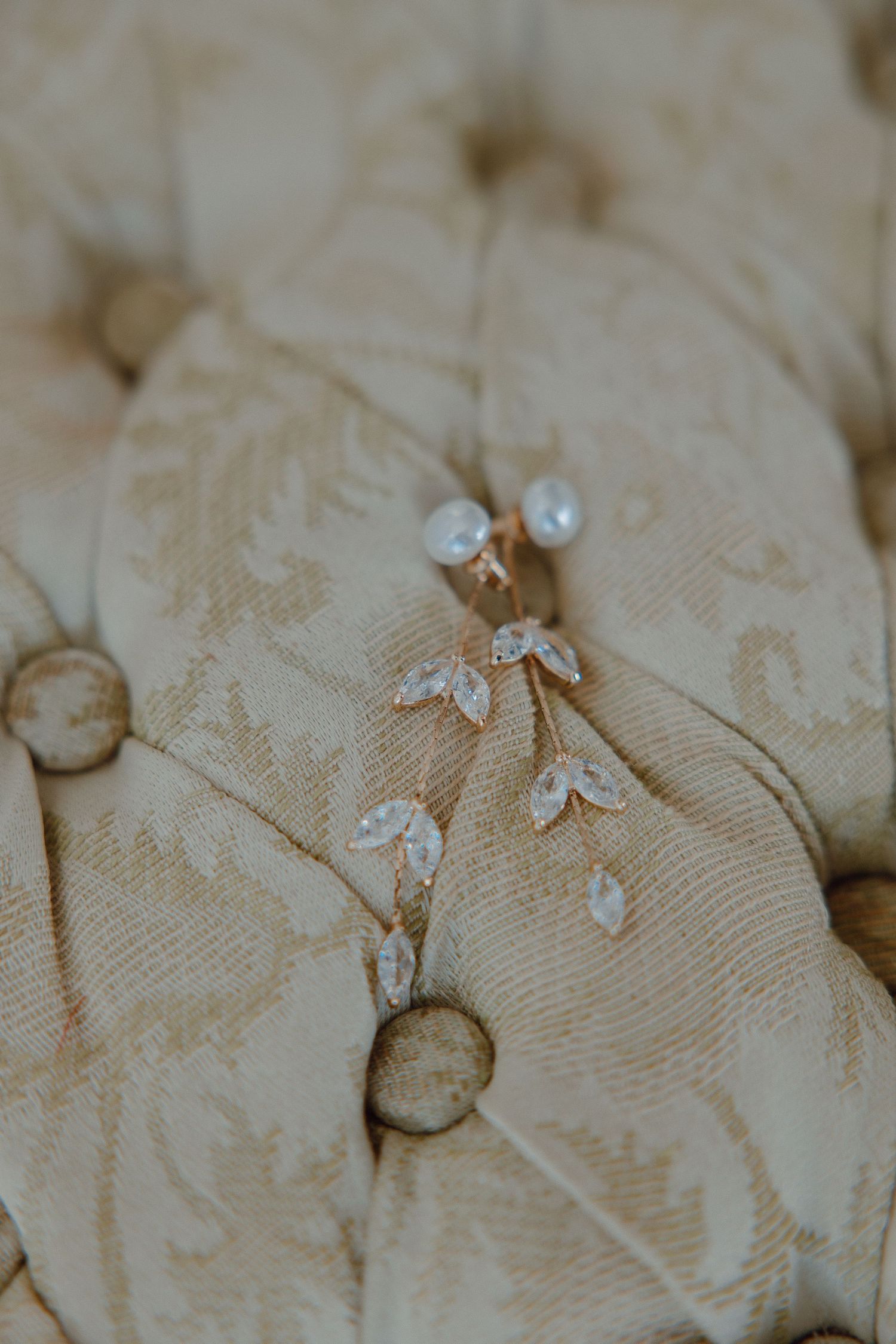 Delicate wedding jewelry and accessories arranged on a textured cream-colored fabric.