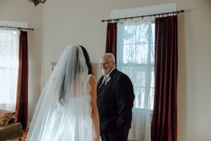 A wedding ceremony taking place in a sunlit room with white curtains and wooden furniture.