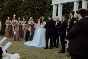 A wide view of a wedding ceremony with guests gathered around white pillars outdoors.