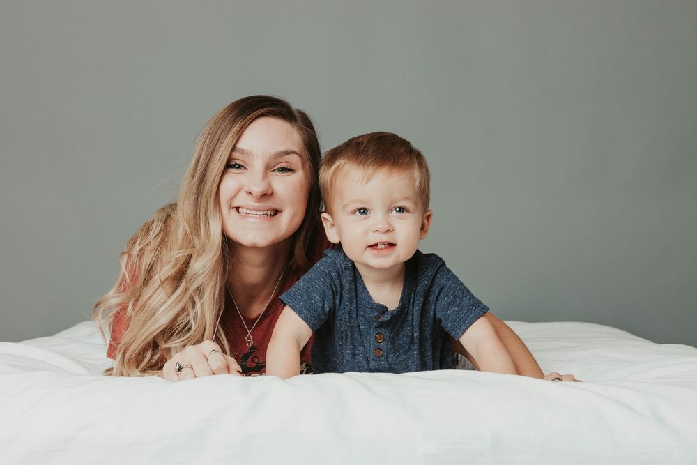 Family photo session with mother and child in casual clothing against grey backdrop.