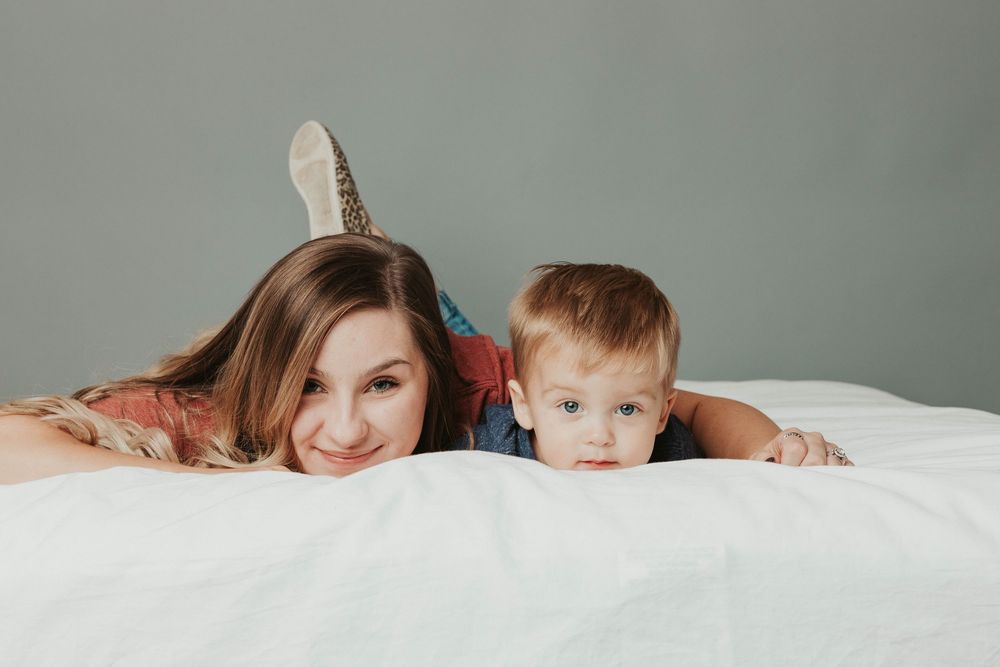 Playful family moment captured in bed with white bedding as they peek out from under the covers together.