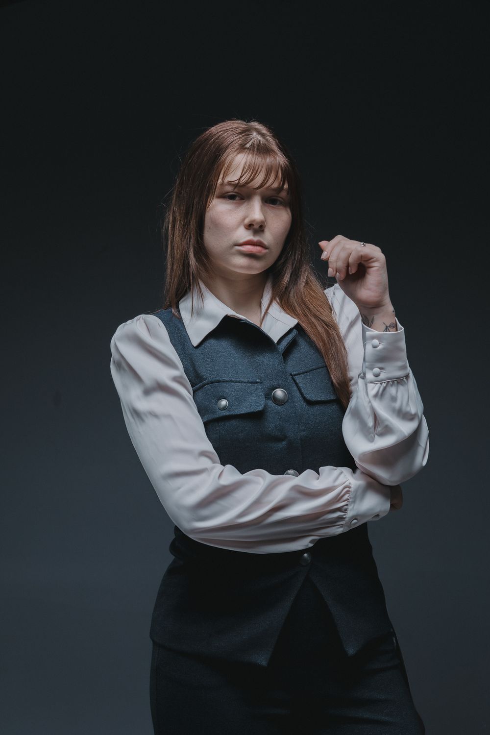 Fashion portrait of a person wearing a white collared shirt and dark vest against a moody dark background.