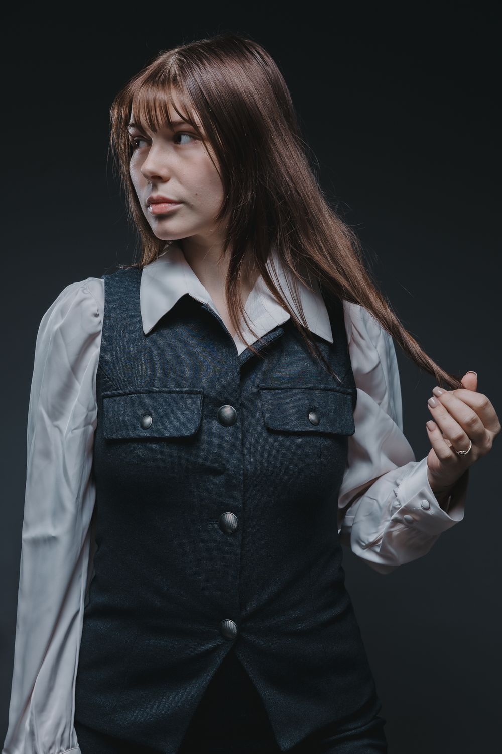 Fashion portrait featuring a dark vest over white blouse against black background.
