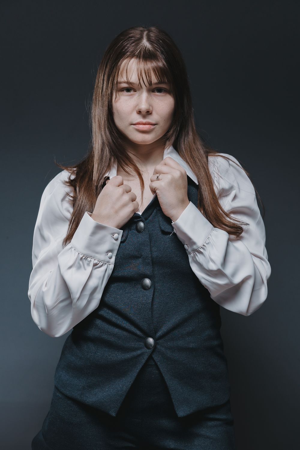 A series of four moody portrait photos showing someone in a dark vest and white blouse against a dark background.