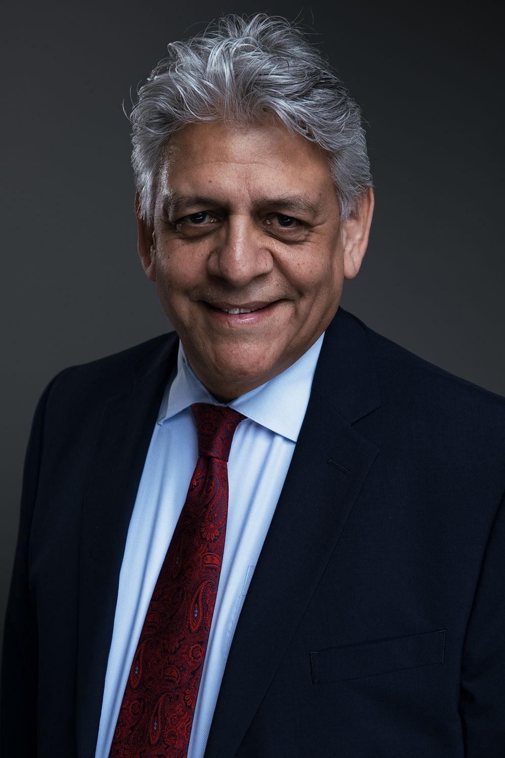 Professional headshot series showing a person in a dark suit and red tie against a black background with varying expressions.