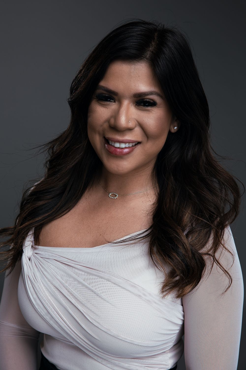 A series of four studio portraits showing someone with dark wavy hair wearing a white wrap top against a gray background.