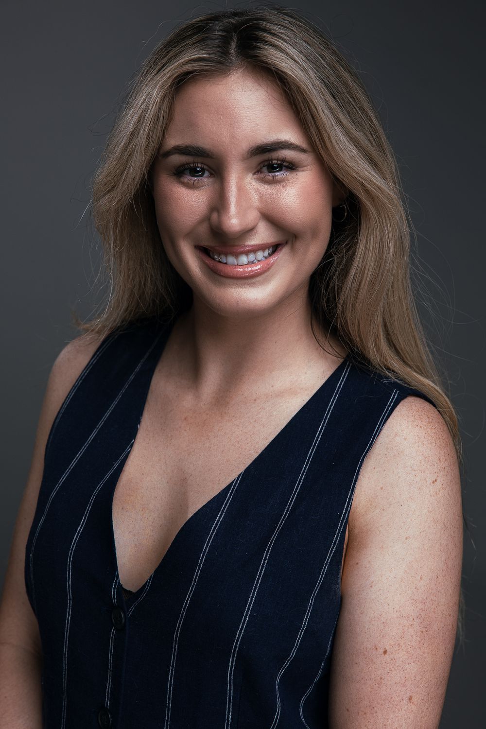 Professional headshot series showing different expressions and poses in a navy sleeveless top against dark background.