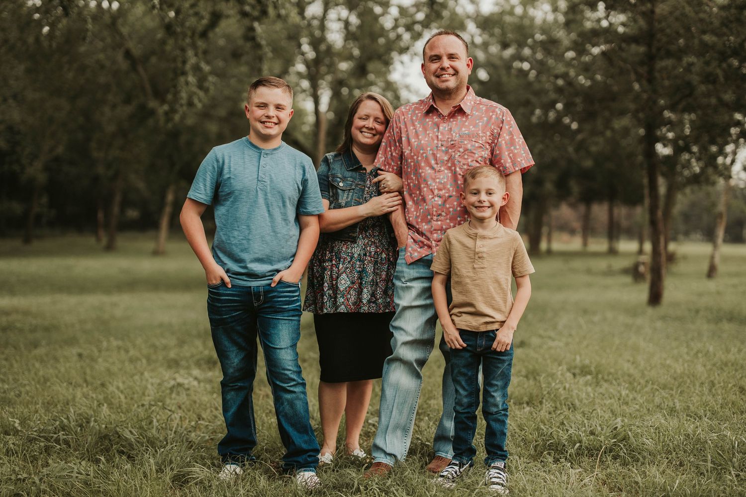 Family of four poses together outdoors in a grassy field during golden hour.
