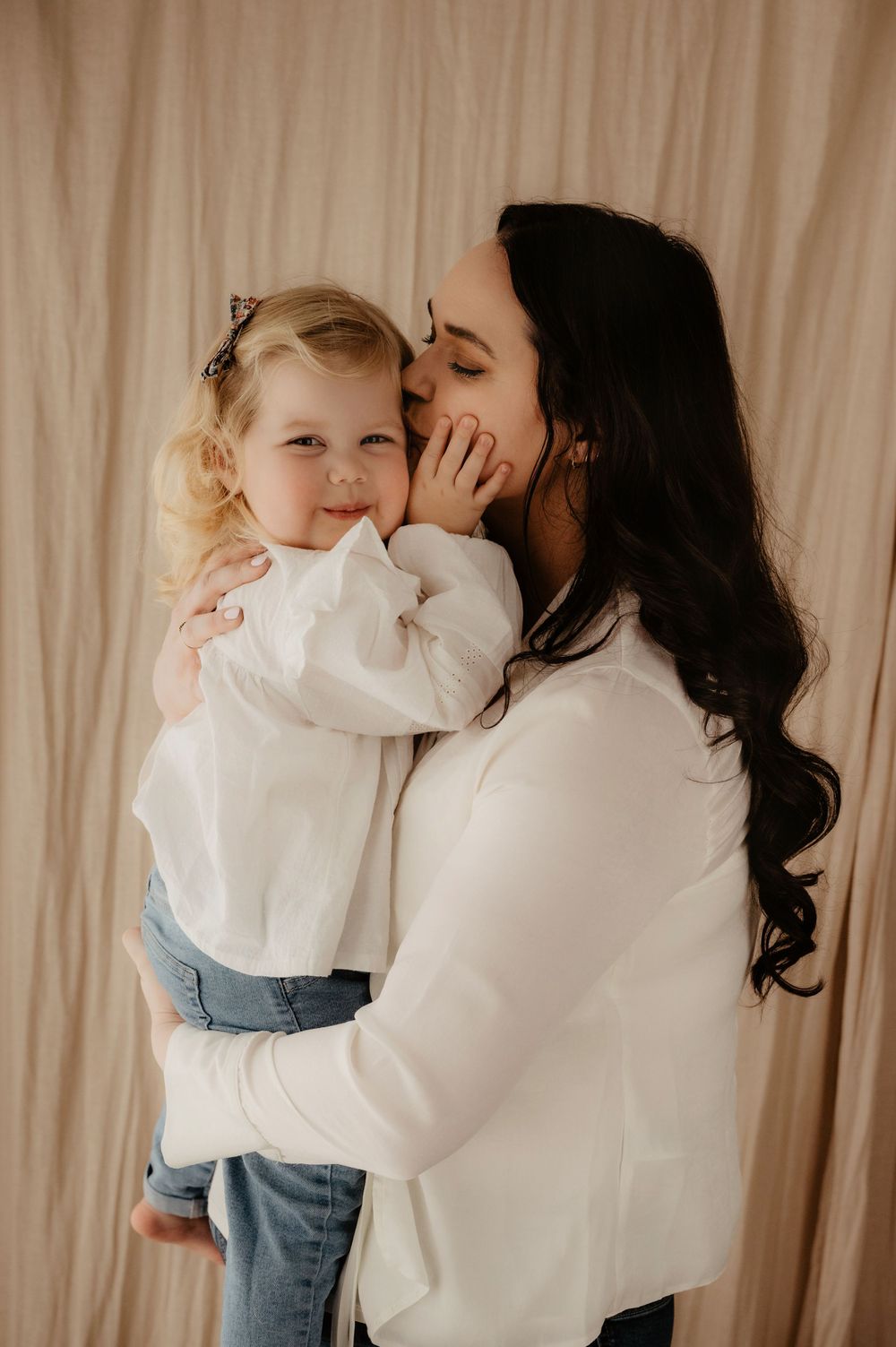 Sweet candid moment of affection against a neutral curtained backdrop.