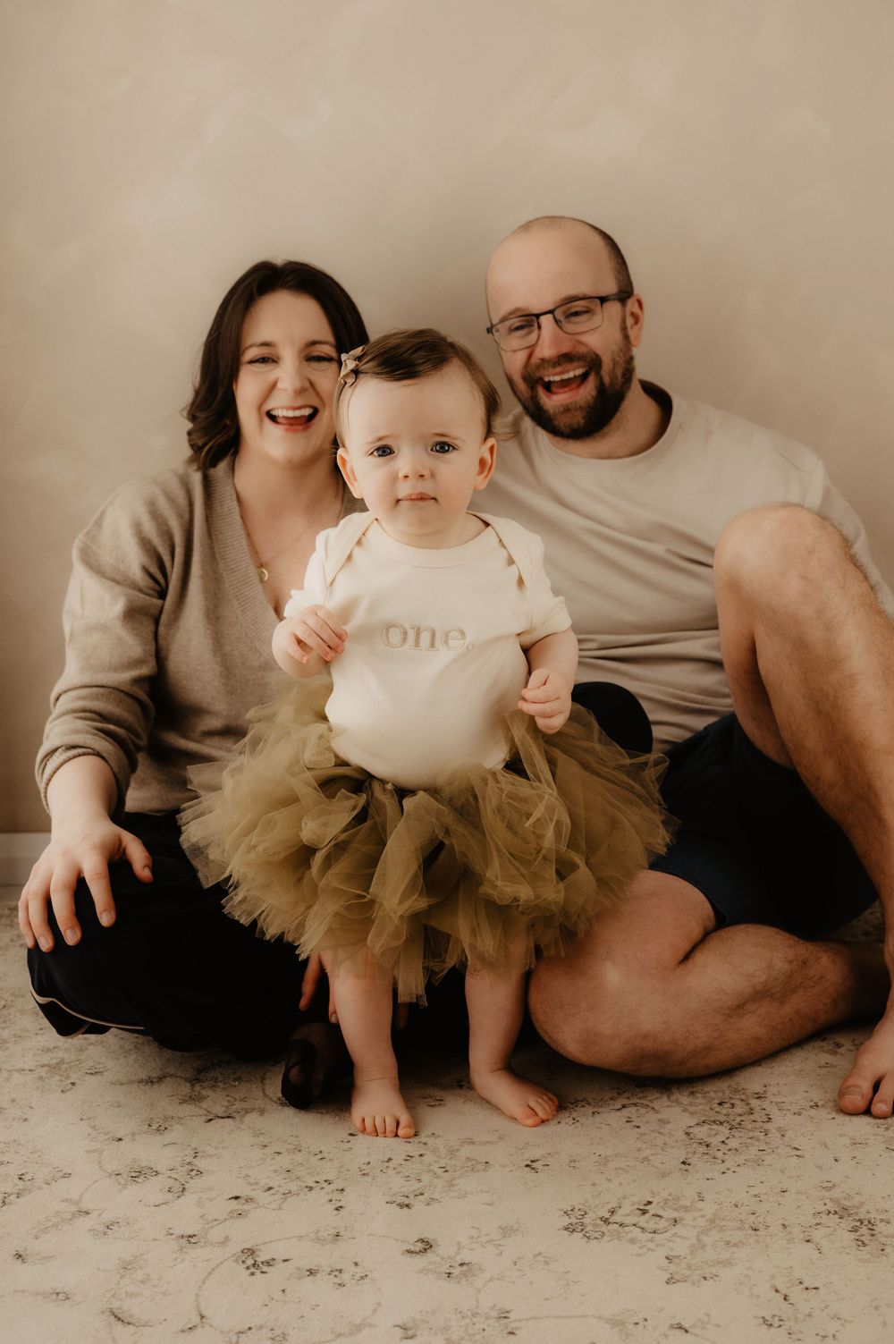 Family portrait with baby wearing tulle skirt against neutral background.